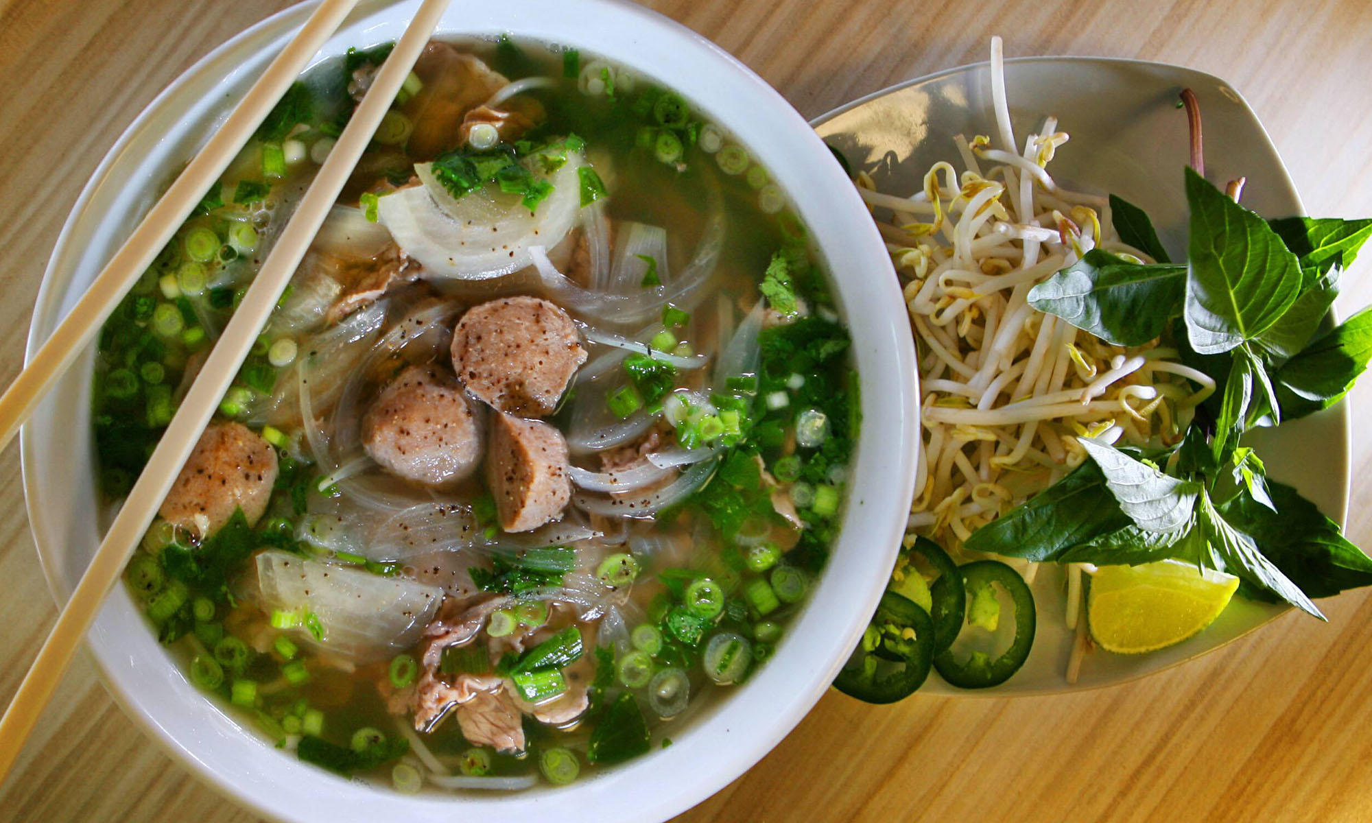 Eine Schale mit Suppe aus Asien, darauf Stäbchen sowie daneben eine Schale mit Sprossen