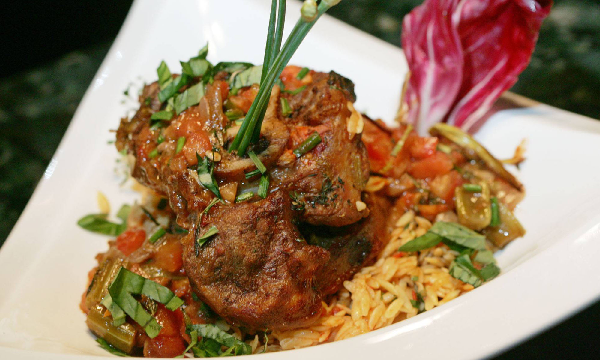 Das italienische Schmorgericht Ossobucco serviert mit kleinen Nudeln auf einem Teller.