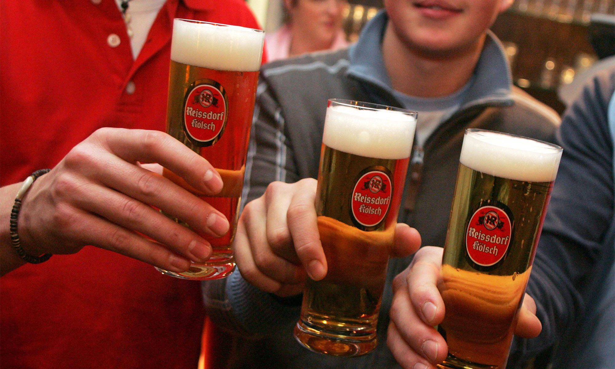 Männer stoßen mit drei Gläsern Kölsch von der Brauerei Reissdorf an