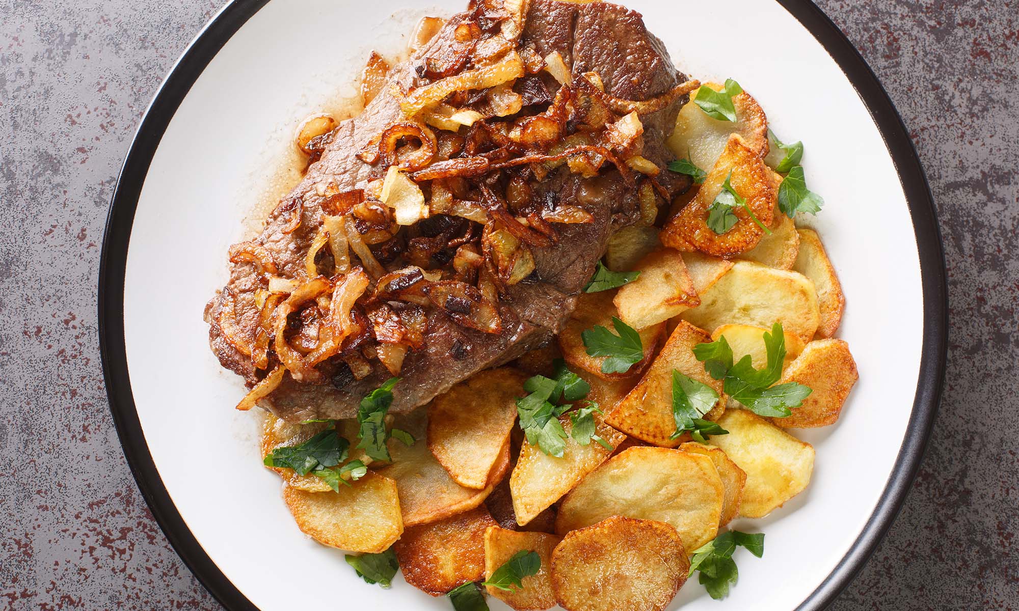 Zwiebelrostbraten Ein Steak mit Zwiebeln, angerichtet auf einem weißen teller mit Bratkartoffeln.