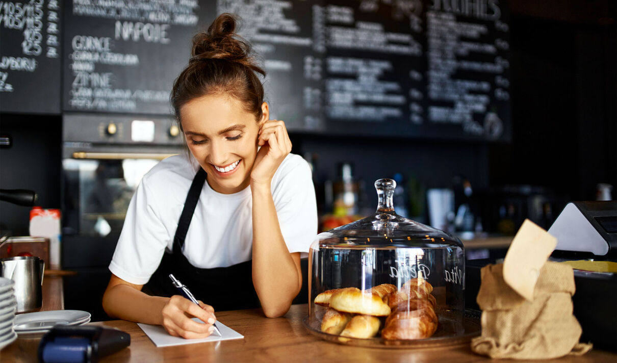 Eine junge Frau an der Verkaufstheke eines Cafés macht sich Notizen