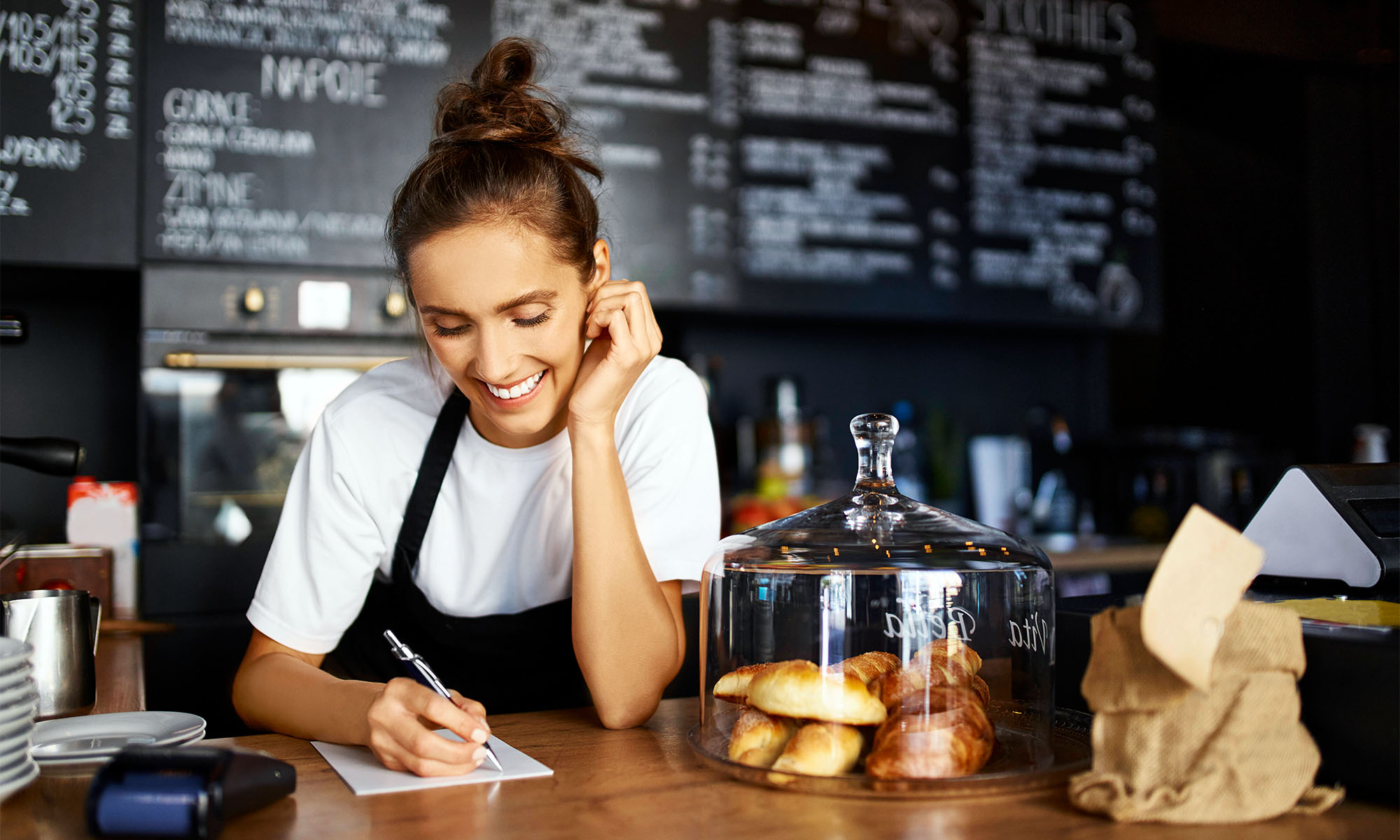 Eine junge Frau an der Verkaufstheke eines Cafés macht sich Notizen