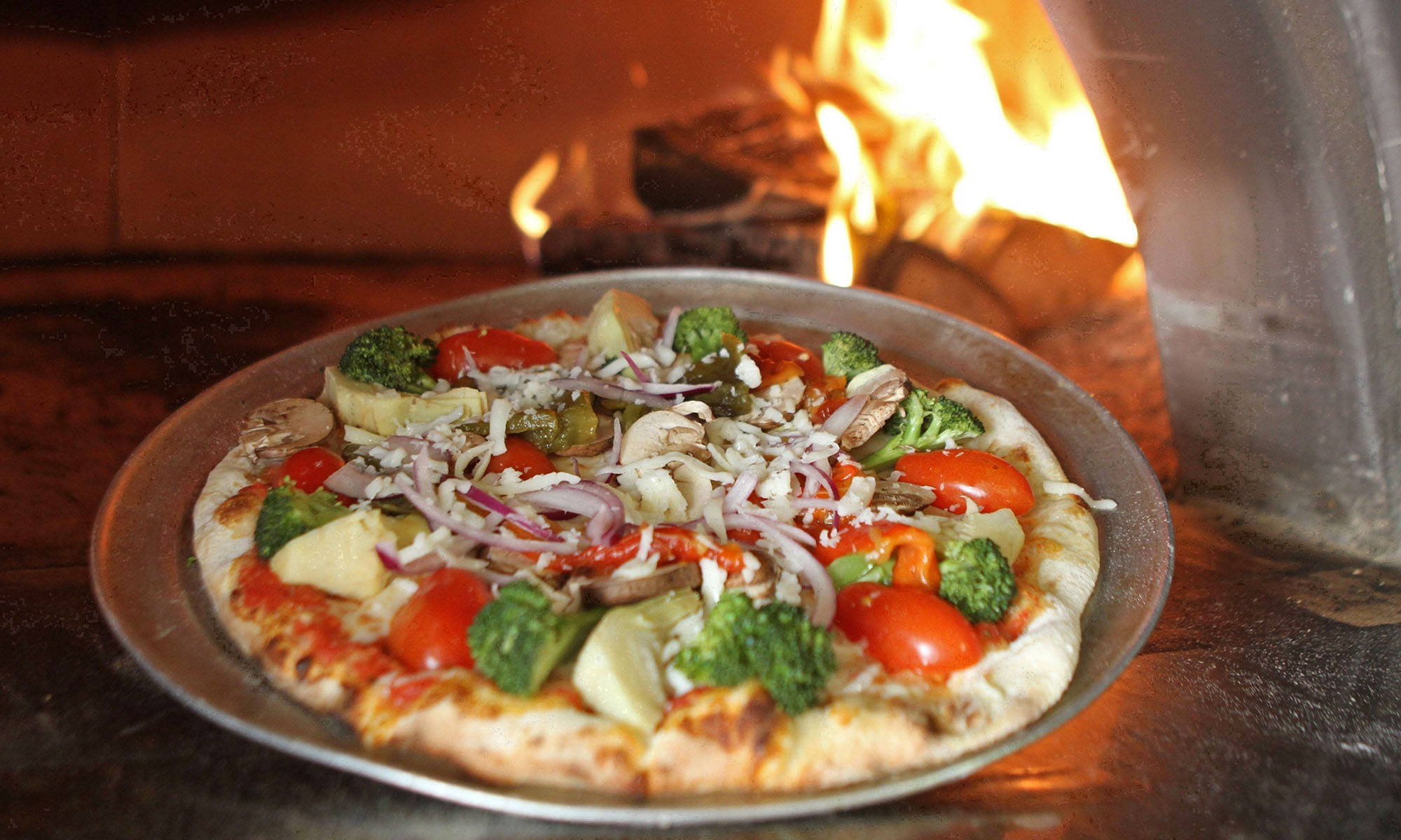 Eine Pizza auf einem Blech wird in einen Ofen mit offener Flamme geschoben