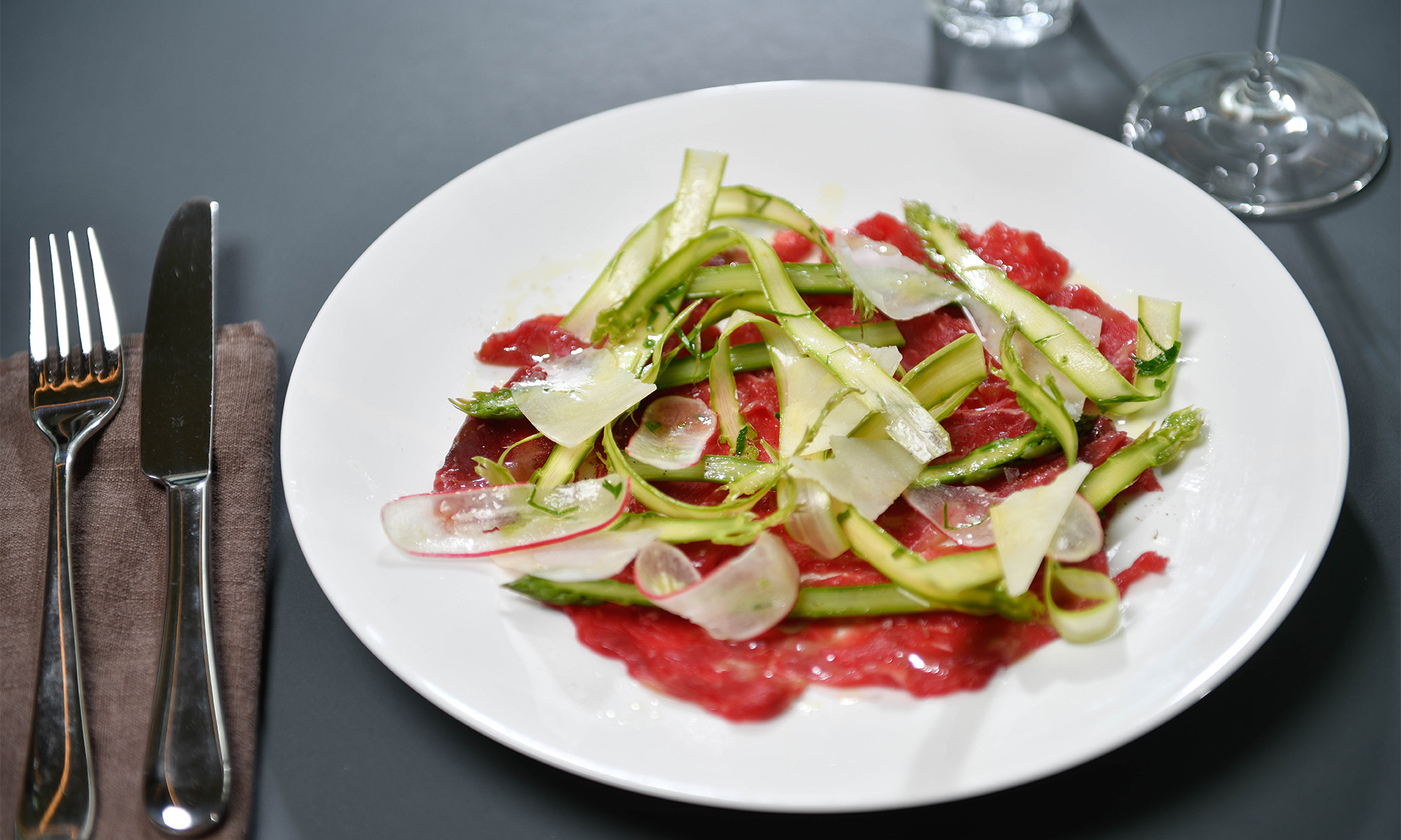 Carpaccio vom Rind mit grünem Spargel und Zitronenvinaigrette auf einem weißen Porzellanteller