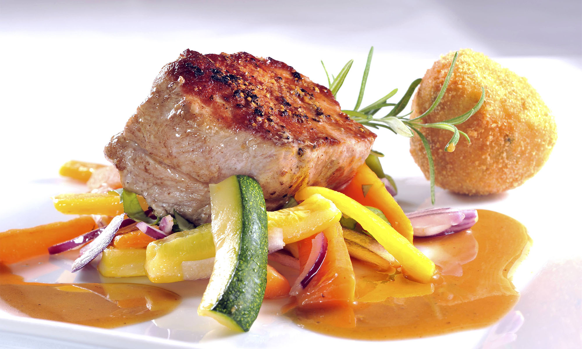 Ein Stück gebratener Kalbsrücken mit Gemüse wie Paprika und Zucchini sowie Arancini