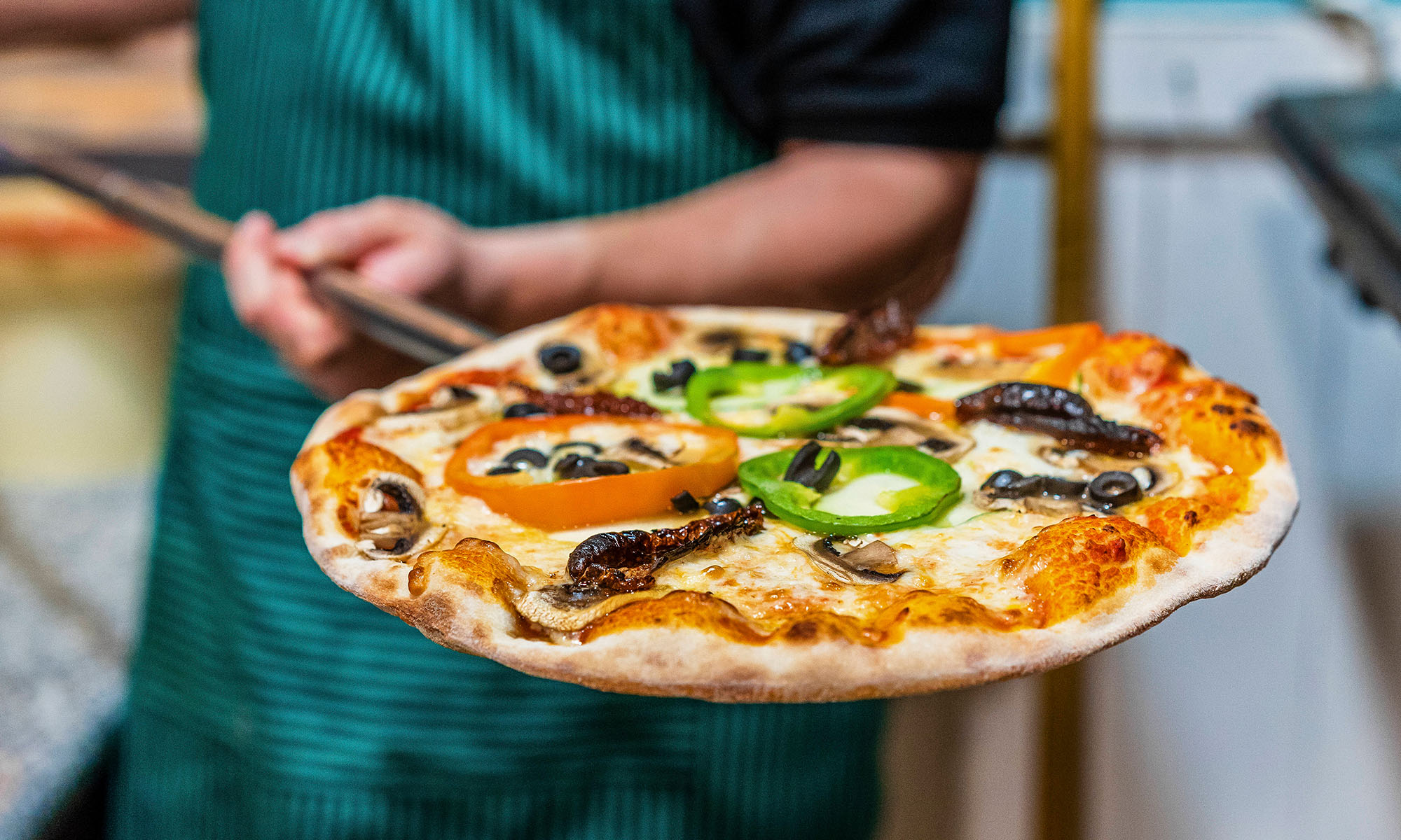 Ein Pizzabäcker holt eine fertige Pizza auf einem Blech aus dem Ofen