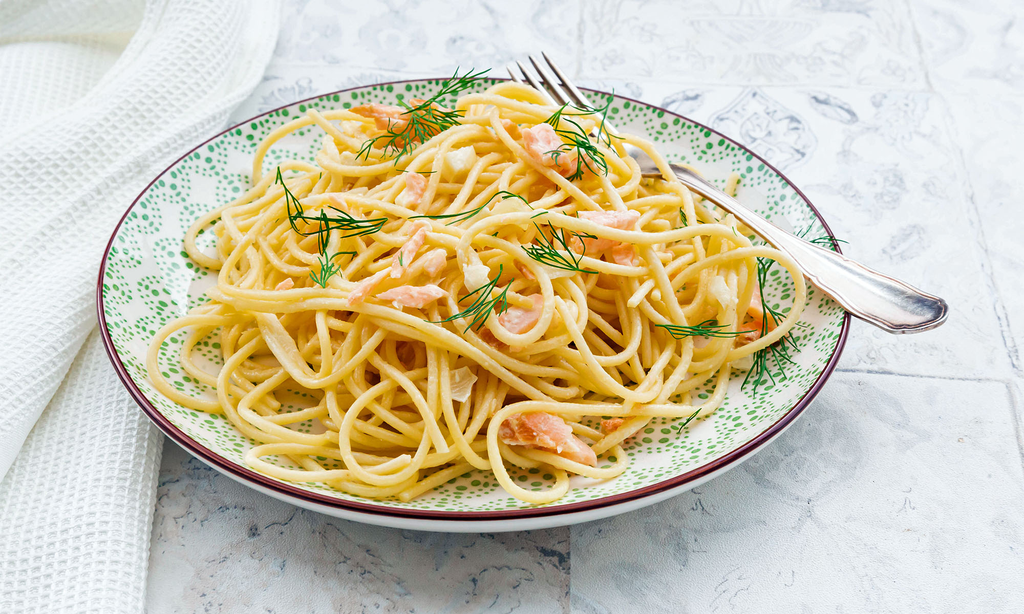 Ein Teller mit Spaghetti mit Lachs, in dem eine Gabel steckt.