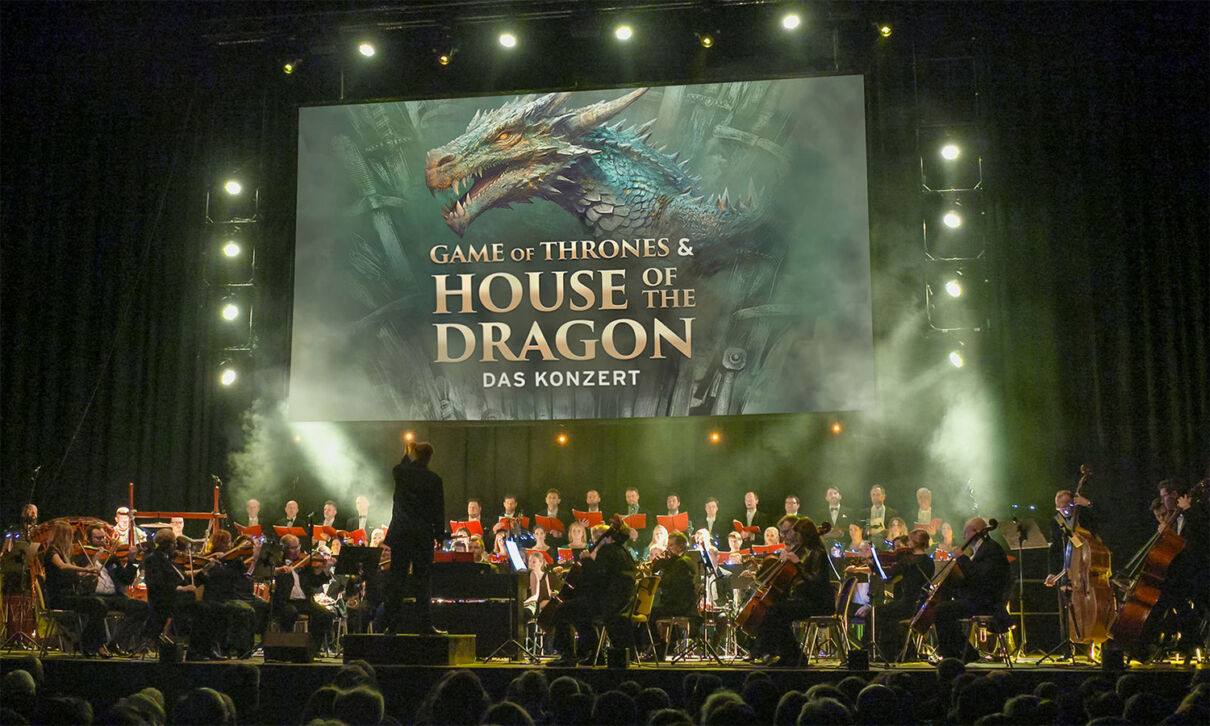 Ein Orchester spielt live die Msuik zu Game of Thrones & House of the Dragon, das auf der Leinwand gezeigt wird.