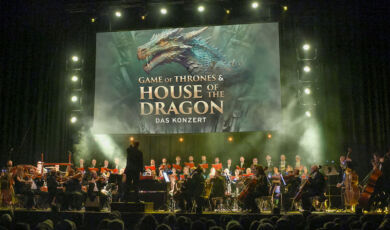 Ein Orchester spielt live die Msuik zu Game of Thrones & House of the Dragon, das auf der Leinwand gezeigt wird.