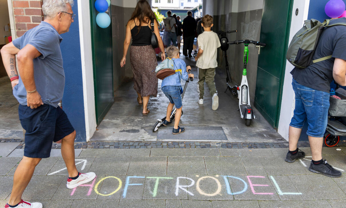 Menschen gehen durch ein Tor, vor dem mit Kreide das Wort Hoftrödel auf das Pflaster geschrieben steht.