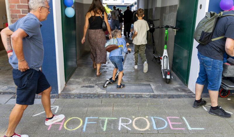 Menschen gehen durch ein Tor, vor dem mit Kreide das Wort Hoftrödel auf das Pflaster geschrieben steht.