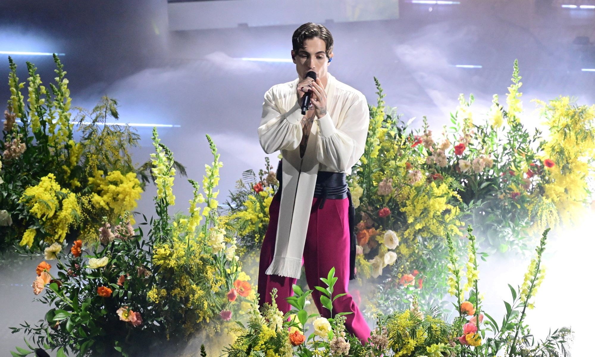 Sänger Damiano David singt bei einem Festival und ist umgeben von zahlreichen Blumen