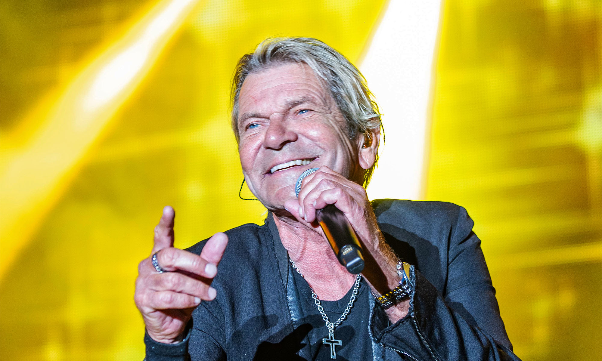 Der Schlagersänger Matthias Reim singt mit einem Mikrofon in der Hand auf einer gelb beleuchteten Bühne