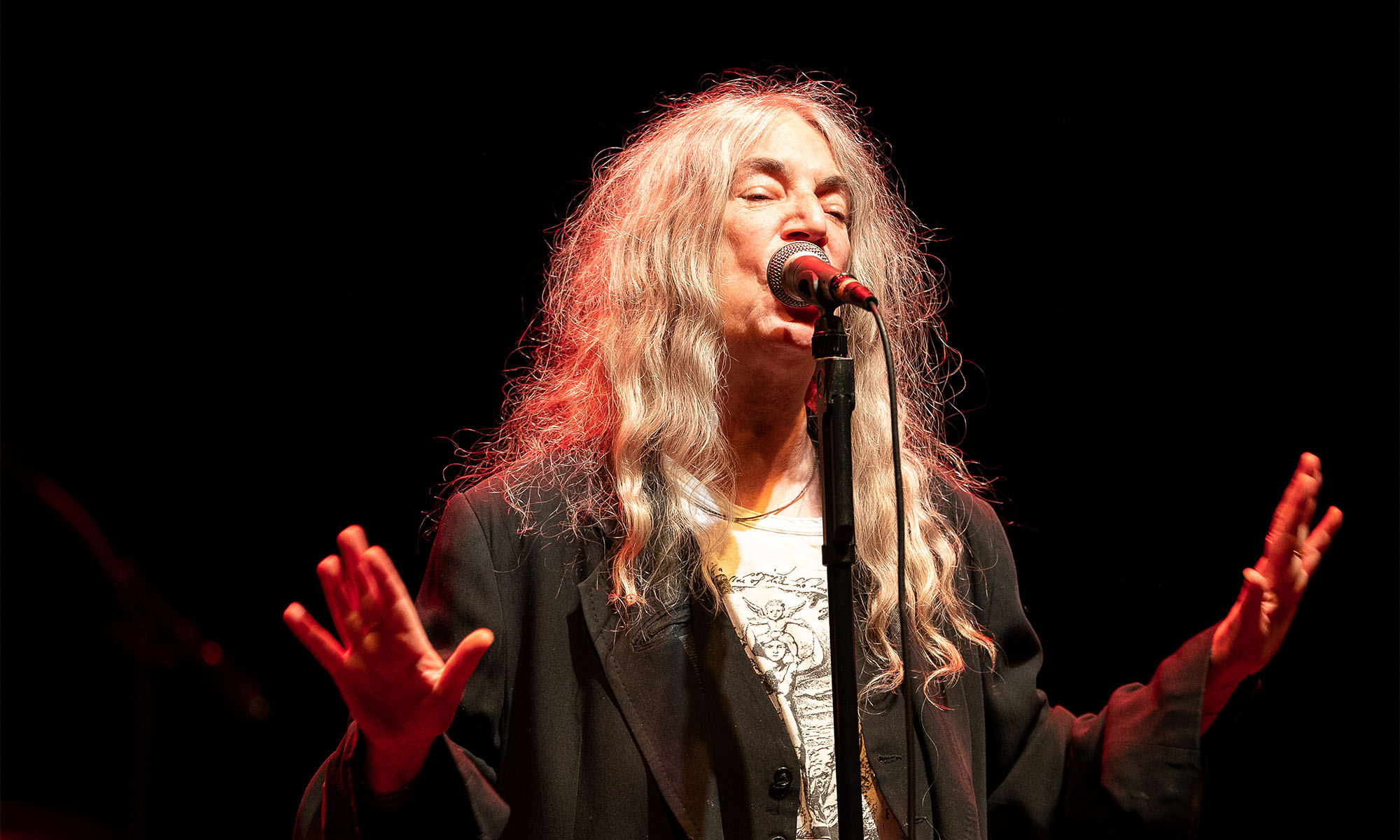 Die Sängerin Patti Smith steht mit ausgebreiteten Armen am Mikrofon.