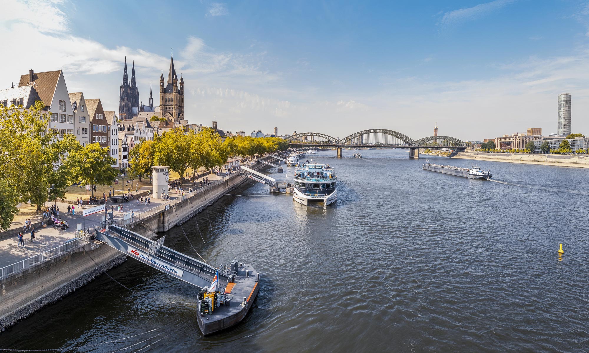 Blick auf das Rheinufer mit Schiffen und der Kölner Altstadt sowie der Hohenzollernbrücke