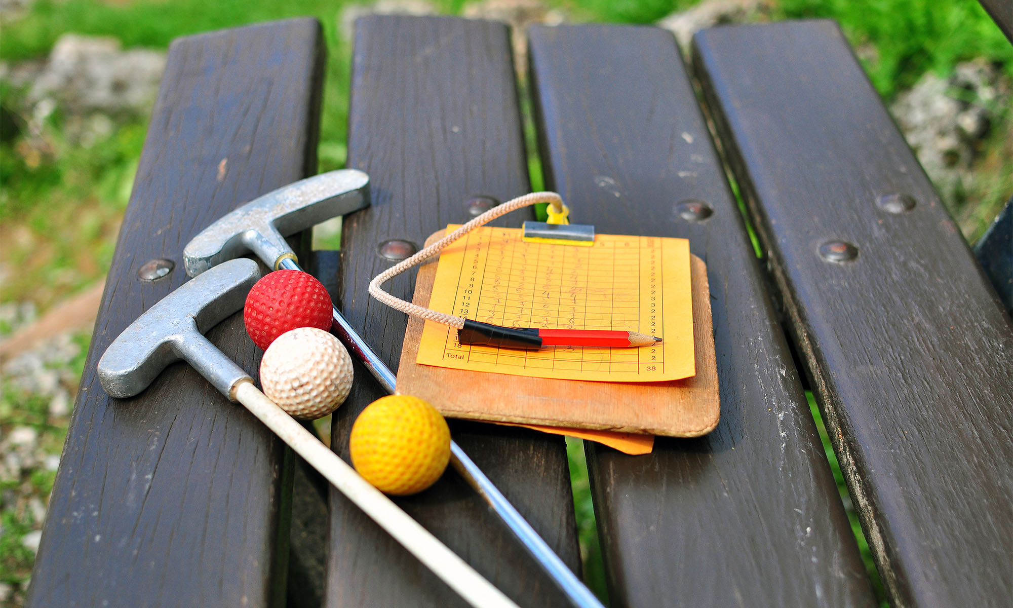 Minigolfschläger, Bälle und Spielblock liegen auf einer Bank