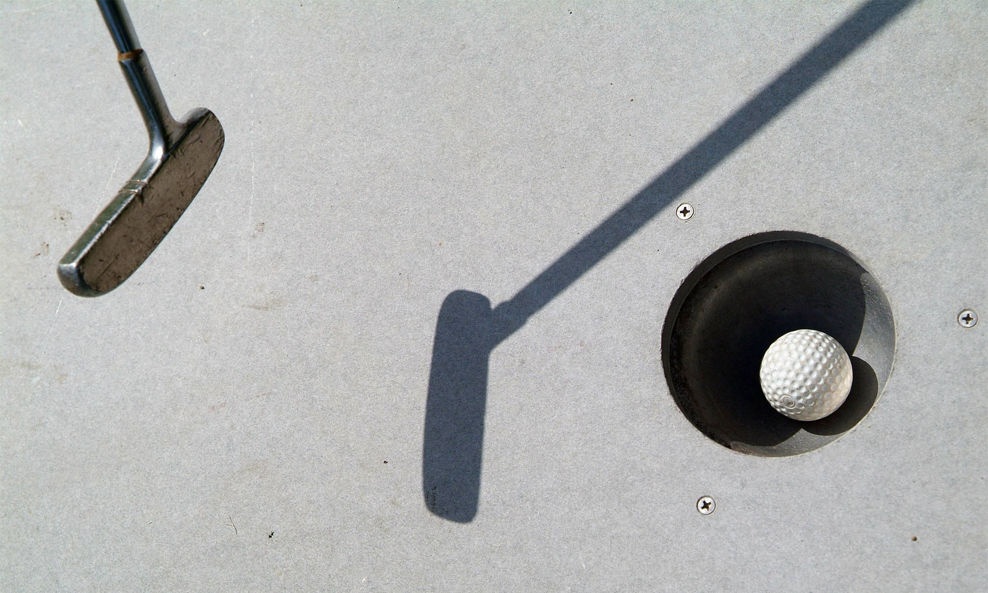 Ein Minigolfschläger wirft einen Schatten auf eine Spielbahn mit einem Ball