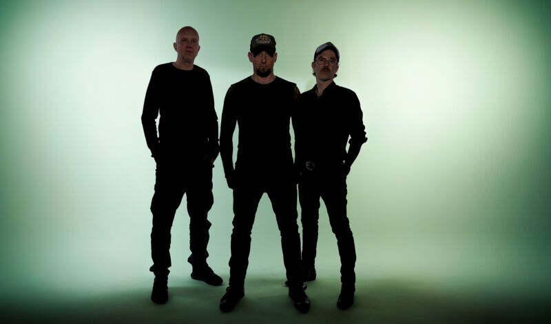 Drei Musiker der Band Volbeat vor einem grünbeleuchteten Hintergrund.