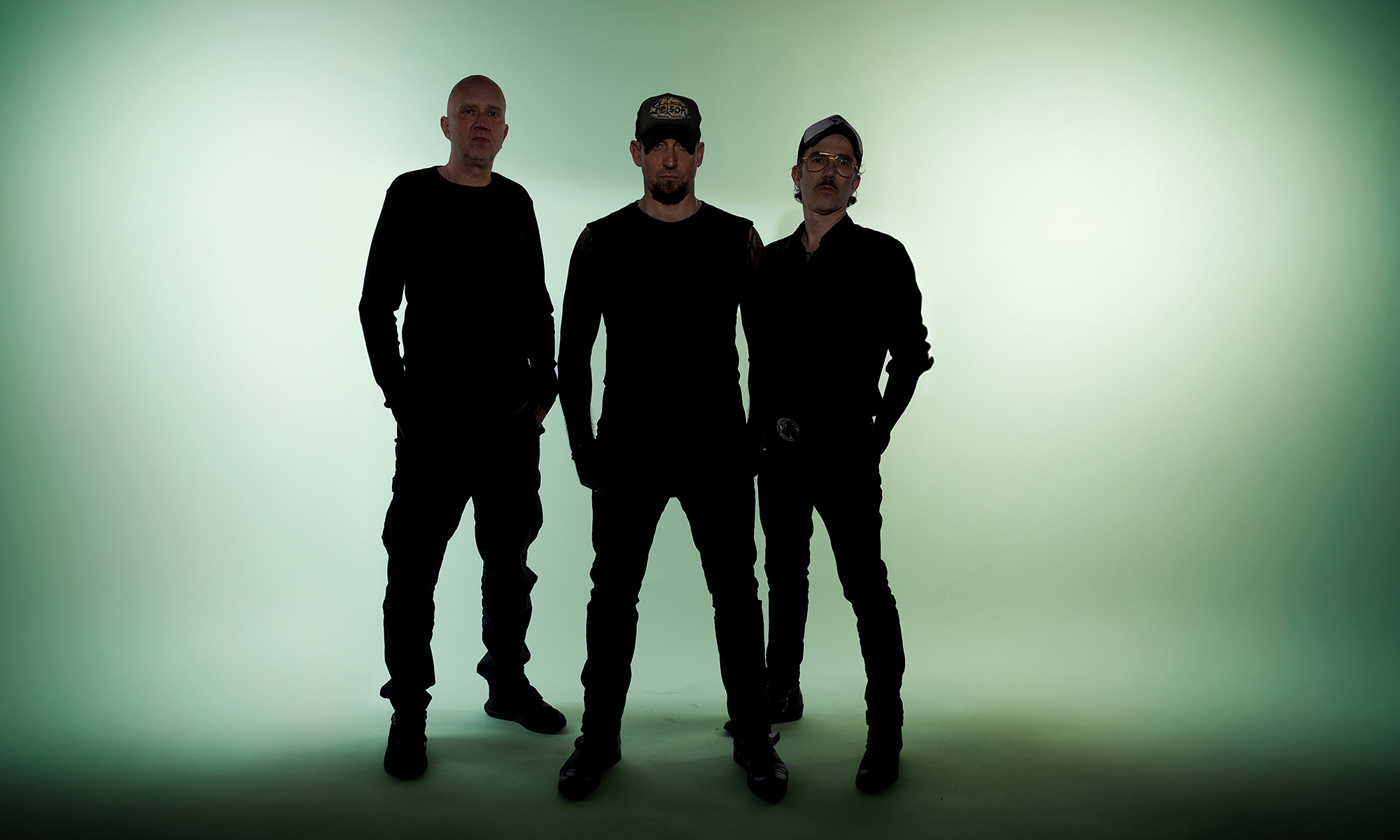 Drei Musiker der Band Volbeat vor einem grünbeleuchteten Hintergrund.