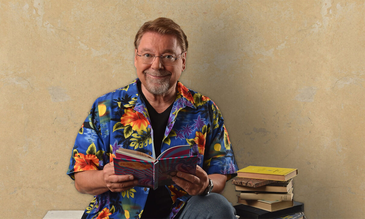 Der Humorist Jürgen von der Lippe sitzt auf Paletten und liest in einem Buch.