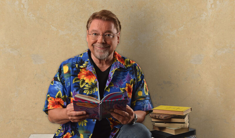 Der Humorist Jürgen von der Lippe sitzt auf Paletten und liest in einem Buch.