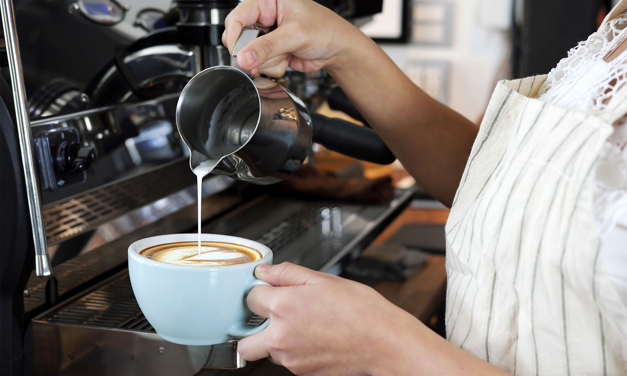 Eine Bedienung gießt aufgeschäumte Milch in eine Tasse und bereitet Cappuccino zu.