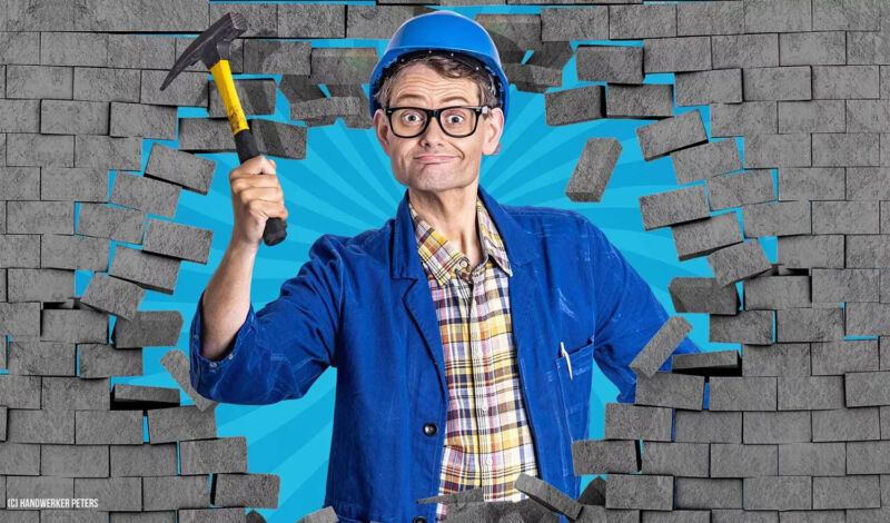 Eine Person mit einem Hammer blicht durch ein Loch im Mauerwerk