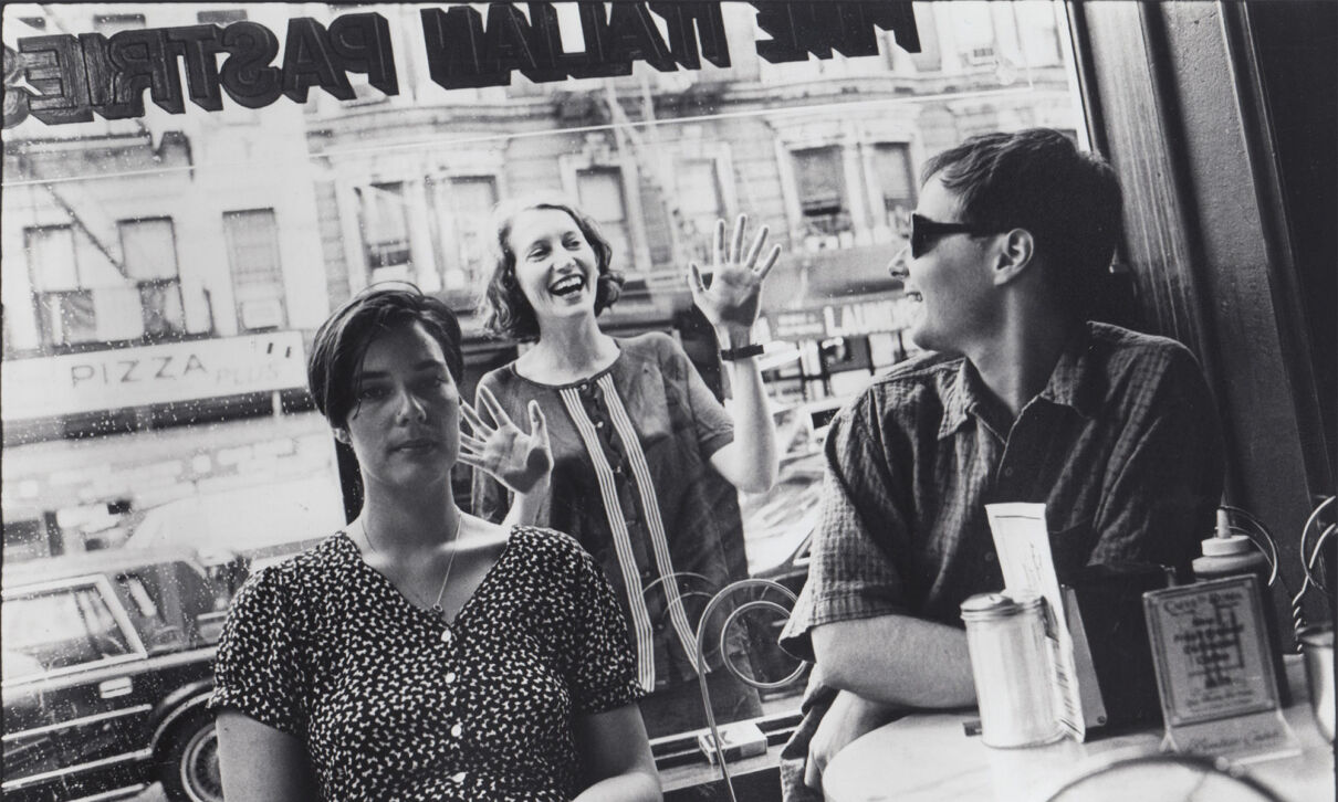 Musiker der britischen Band Stereolab sitzen in inem Cafè, ein Bandmitglied sieht von draußen durch das Fenster herein.