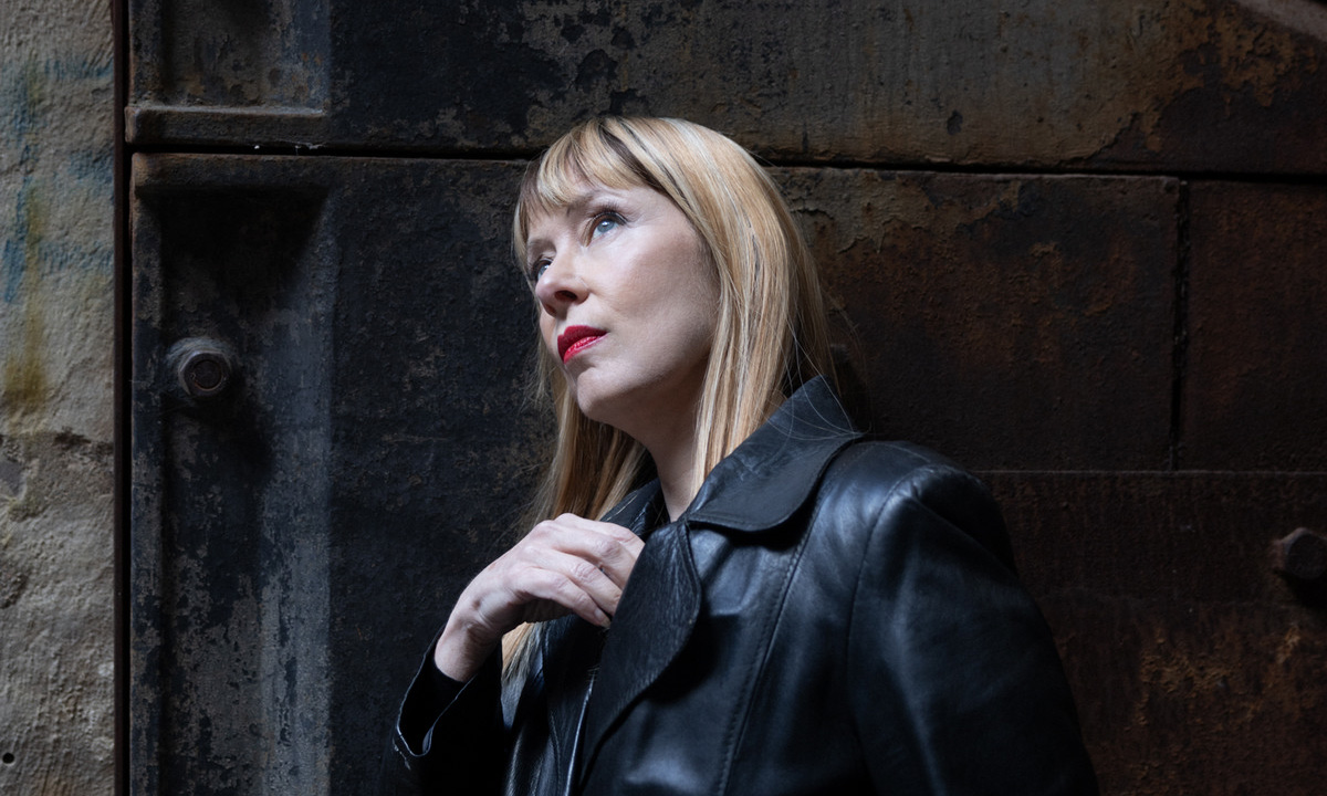 Die amerikanische Sängerin Suzanne Vega in einem schwarzen Mantel vor einem dunklen Hintergrund