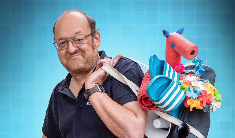 Comedian Robbi Pawlik alias Bademeister Schaluppke im blauen Polohemd mit einem Beutel voller Strandutensilien.