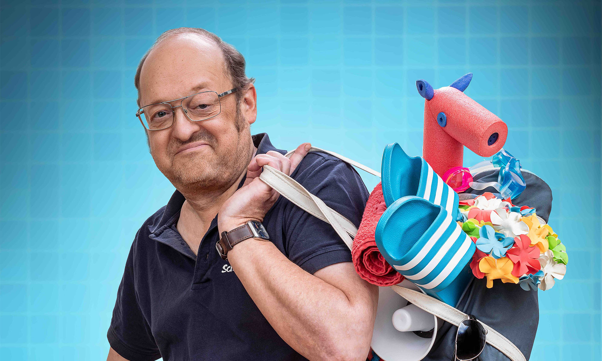 Comedian Robbi Pawlik alias Bademeister Schaluppke im blauen Polohemd mit einem Beutel voller Strandutensilien.