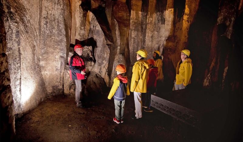 Eine Gruppe Personen mit Helmen hören einem Guide in einer Höhle zu.