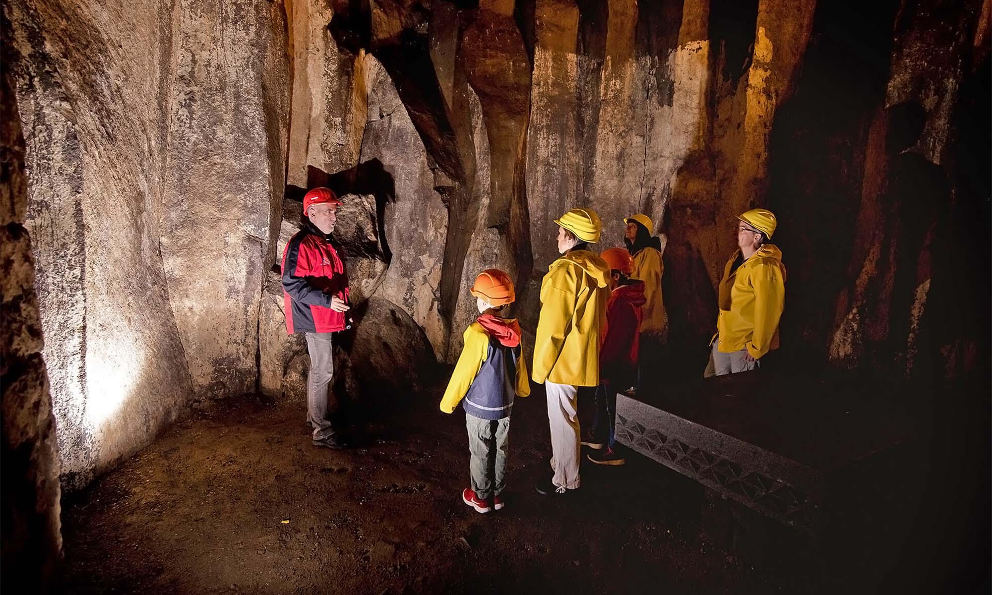 Eine Gruppe Personen mit Helmen hören einem Guide in einer Höhle zu.