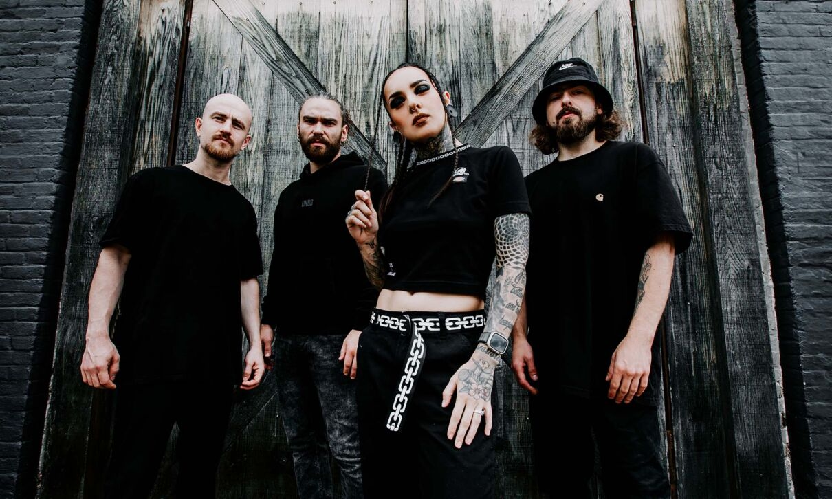 Die Mitglieder der Metalband Jinjer stehen schwarz gekleidet vor einer Holzwand.