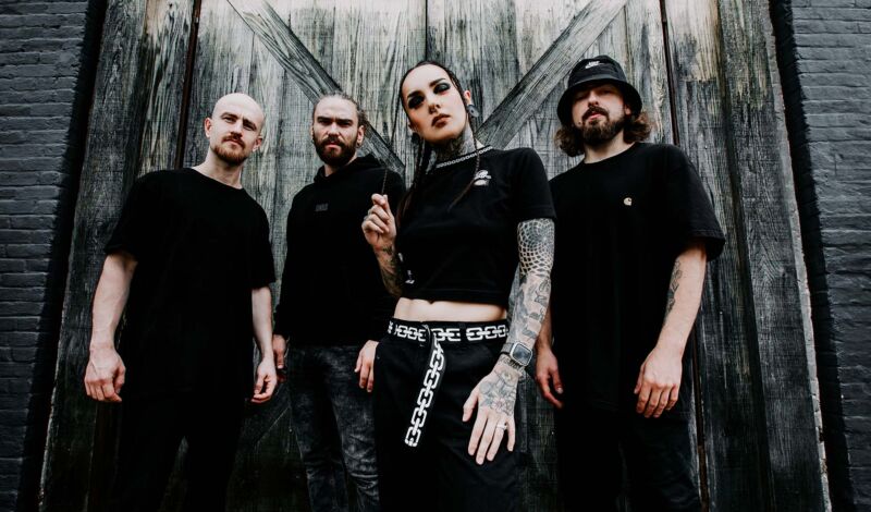 Die Mitglieder der Metalband Jinjer stehen schwarz gekleidet vor einer Holzwand.