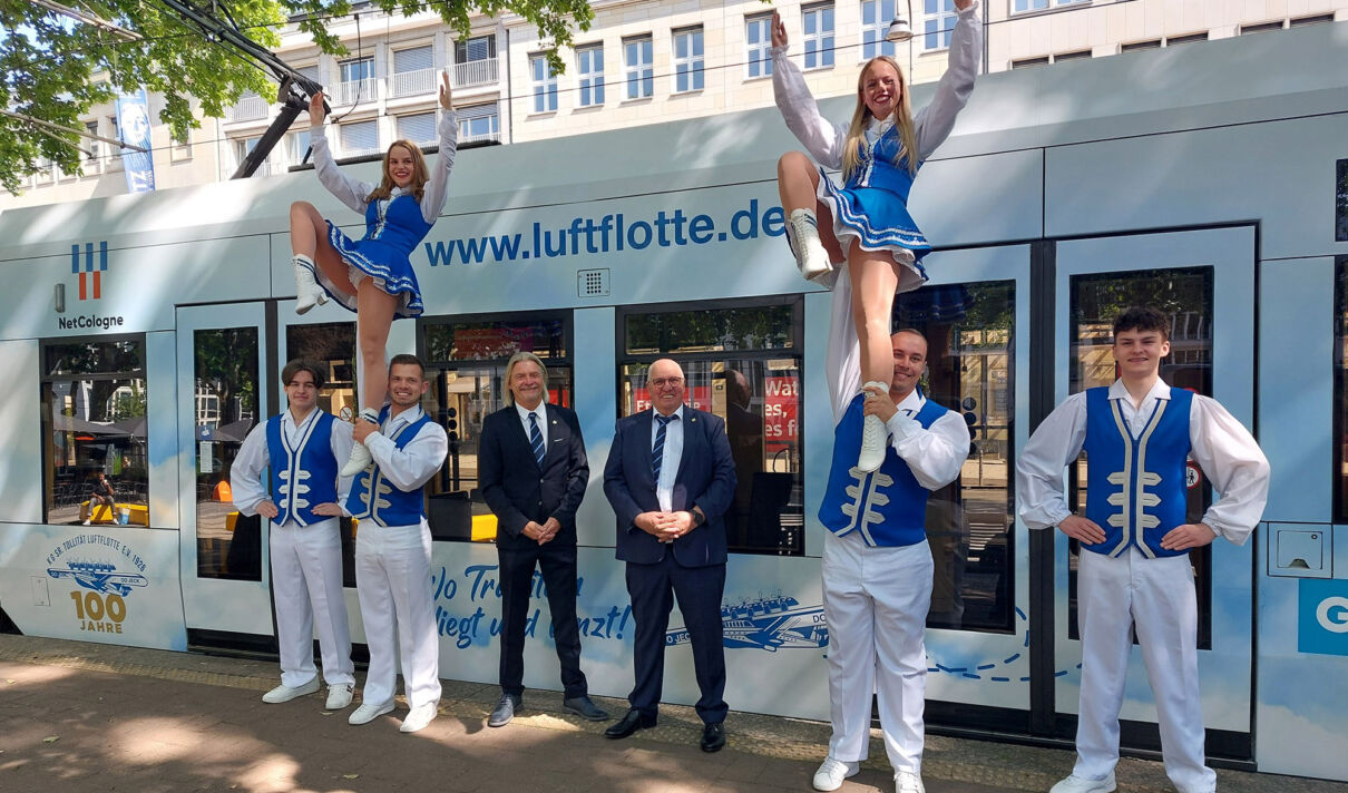 Mitglieder der KG Lusftflotte posieren vor einer KVB-Bahn im Luftflotten-Design