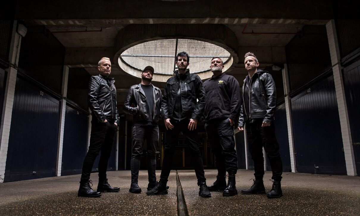 Musiker der australischen Elektronikband Pendulum stehen in einer dunklen Fabrikhalle.
