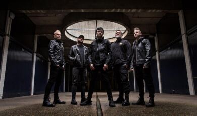 Musiker der australischen Elektronikband Pendulum stehen in einer dunklen Fabrikhalle.