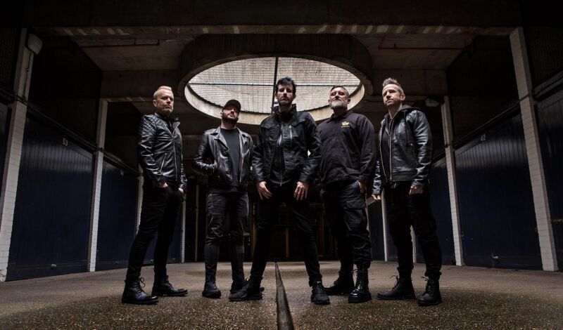 Musiker der australischen Elektronikband Pendulum stehen in einer dunklen Fabrikhalle.