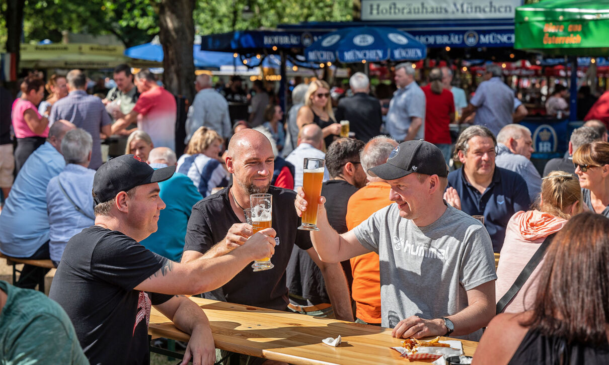 Mehrere Männer sitzen an Biertischen und stoßen auf einer Bierbörse mit Weßbier an