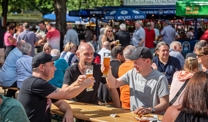 Mehrere Männer sitzen an Biertischen und stoßen auf einer Bierbörse mit Weßbier an