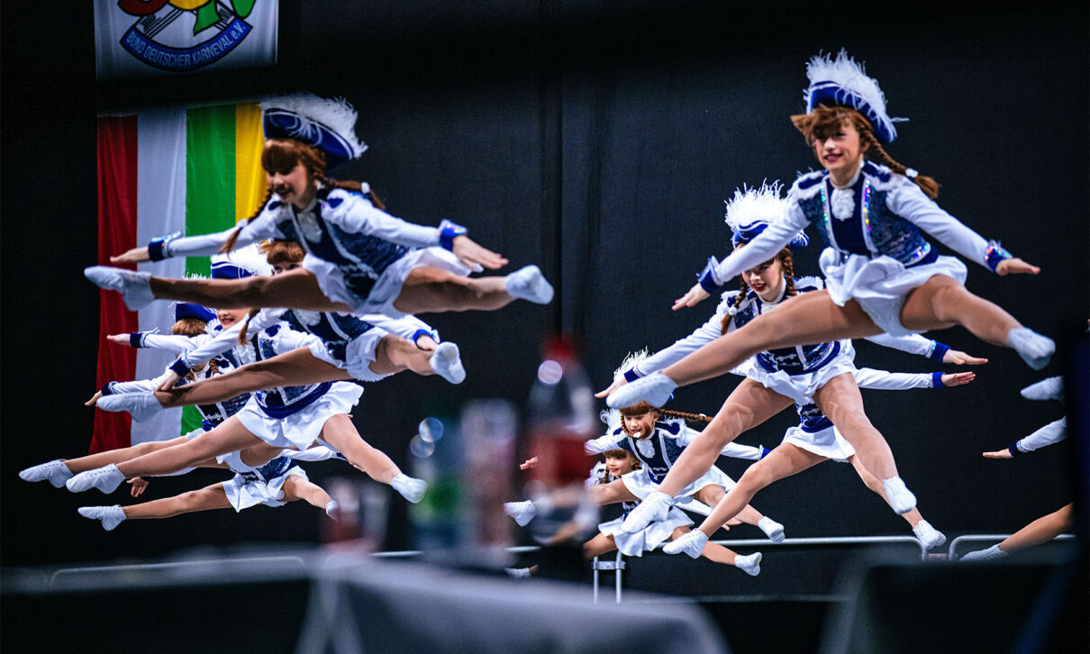 Mehrere Funkenmariechen springen während eines Tanzes im Spagat in die luft.