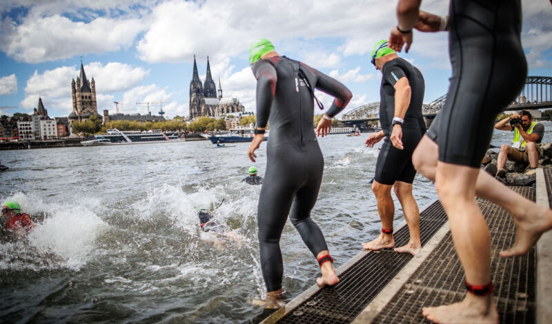 Schwimmer im Neoprenanzug am Start des Schwimmwettbewerbs des Köln-Triathlons mit Dem Altstadtpanorama im Hintergrund.