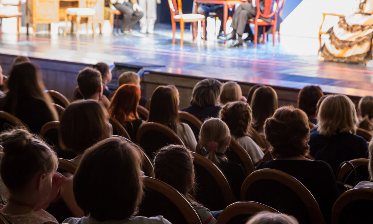 Blick über das Publikum auf die Bühne einer Theateraufführung.