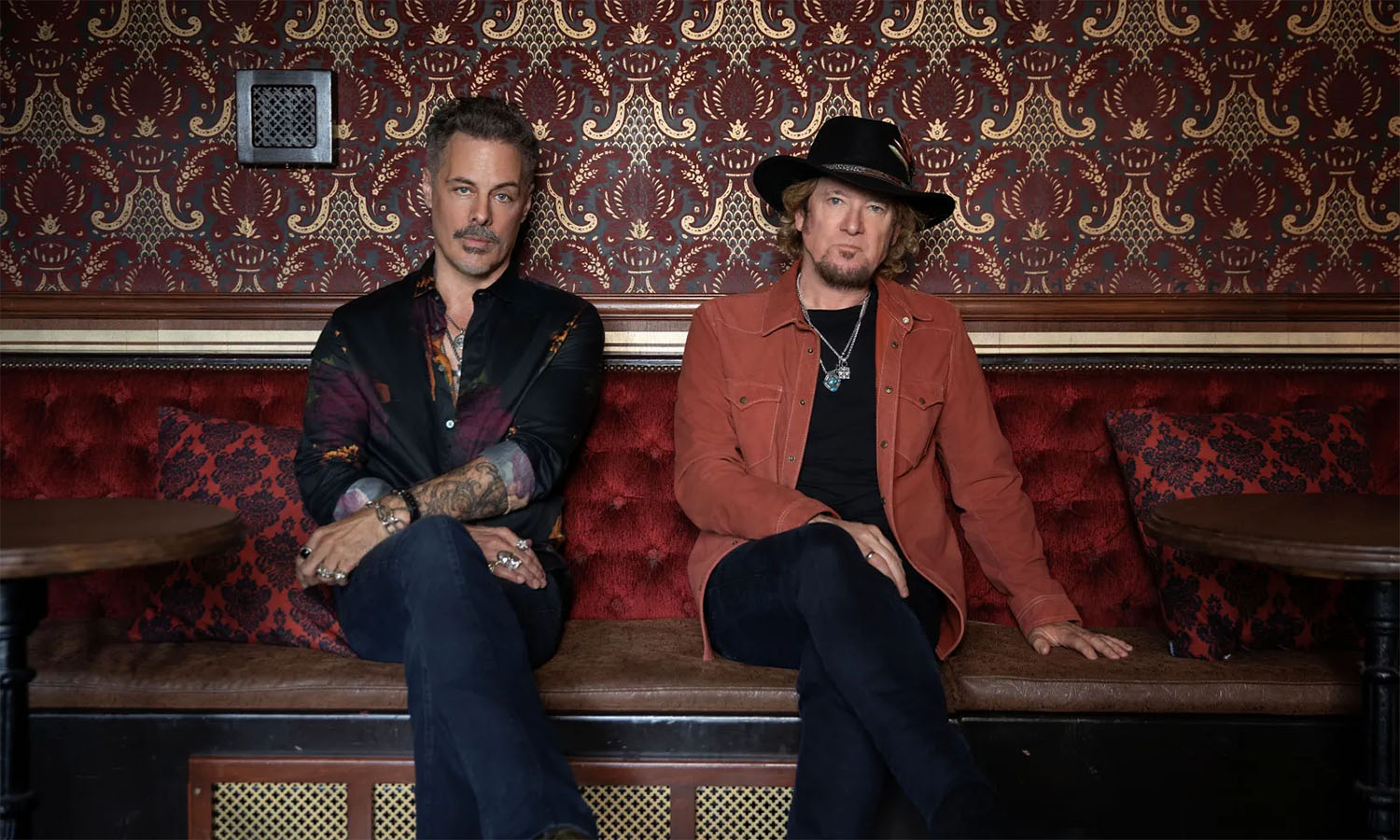 Die beiden Rockmusiker Richie Kotzen und Adrian Smith sitzen auf einer Bank.