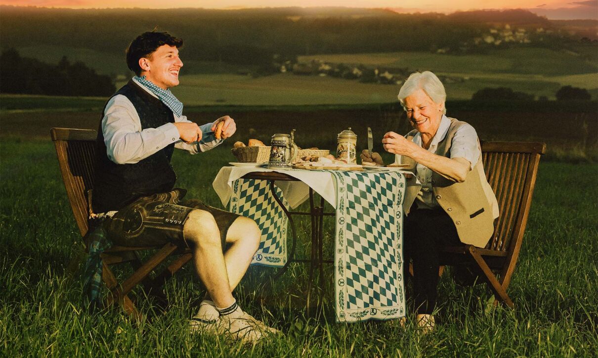 Der Rapper Tream sitzt gemeinsam mit einer Frau an einem Tisch auf einer Wiese.