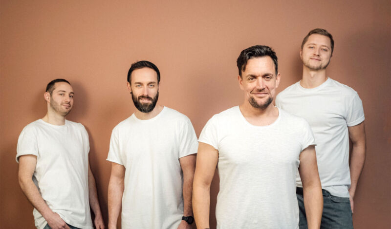 Die vier Musiker der Kölner Band Fiasko in weißen T-Shirts vor einem braunen Hintergrund