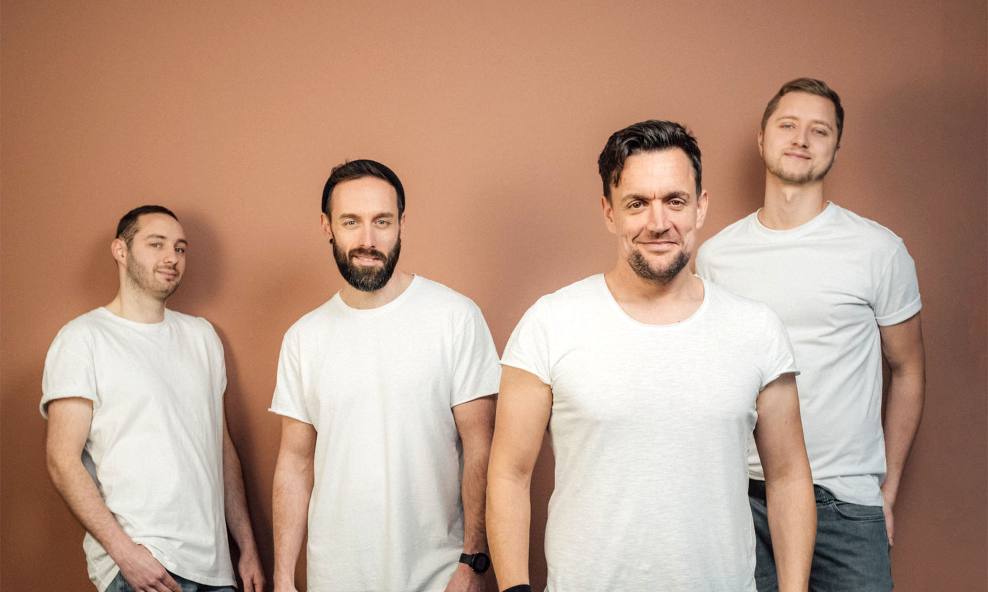 Die vier Musiker der Kölner Band Fiasko in weißen T-Shirts vor einem braunen Hintergrund