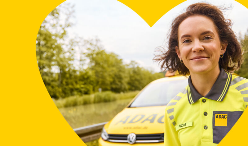 Das Foto zeigt eine Mitarbeiterin des ADAC vor ihrem gelben Einsatzfahrzeug