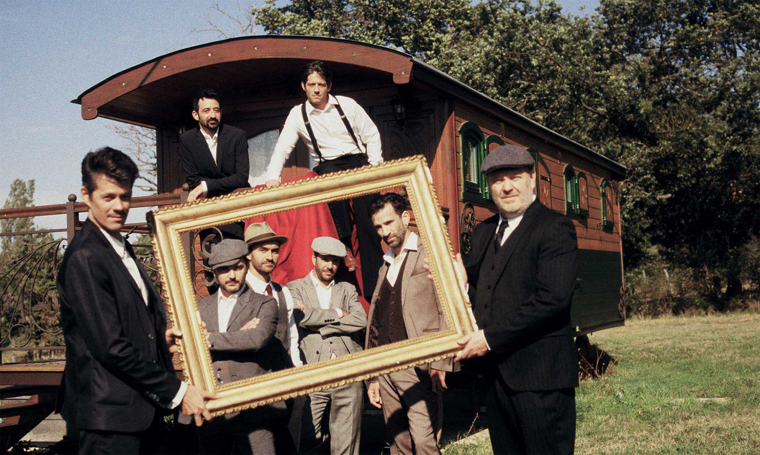 Die Musiker der Band Babylon Circus stehen vor einem Pferdewagen und halten einen Bilderrahmen in der Hand.